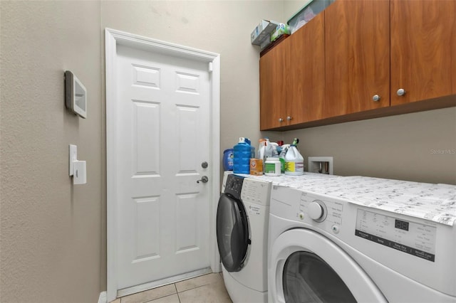 laundry area featuring washing machine and clothes dryer, light tile patterned floors, and cabinets