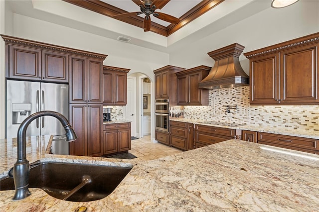 kitchen featuring premium range hood, sink, decorative backsplash, appliances with stainless steel finishes, and light stone countertops