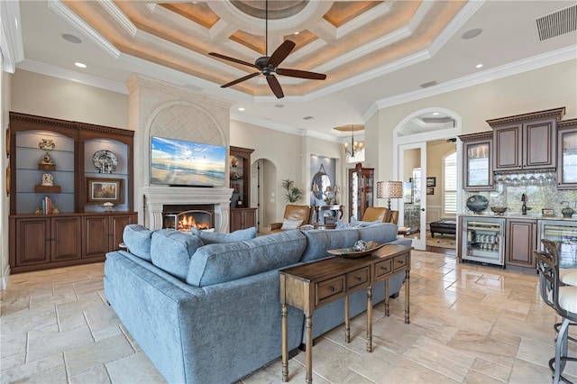 living room featuring beverage cooler, coffered ceiling, crown molding, a tray ceiling, and a fireplace