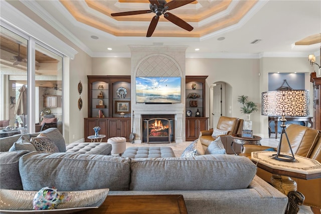 living room with a raised ceiling, crown molding, a fireplace, and ceiling fan