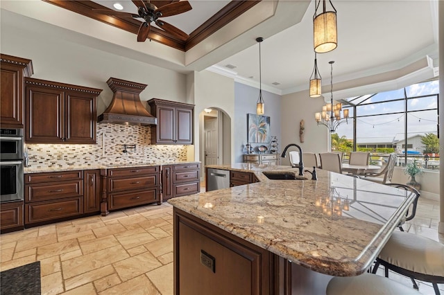 kitchen with a kitchen breakfast bar, custom exhaust hood, sink, hanging light fixtures, and a large island