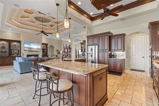 kitchen featuring stainless steel refrigerator with ice dispenser, a tray ceiling, a breakfast bar, a spacious island, and hanging light fixtures