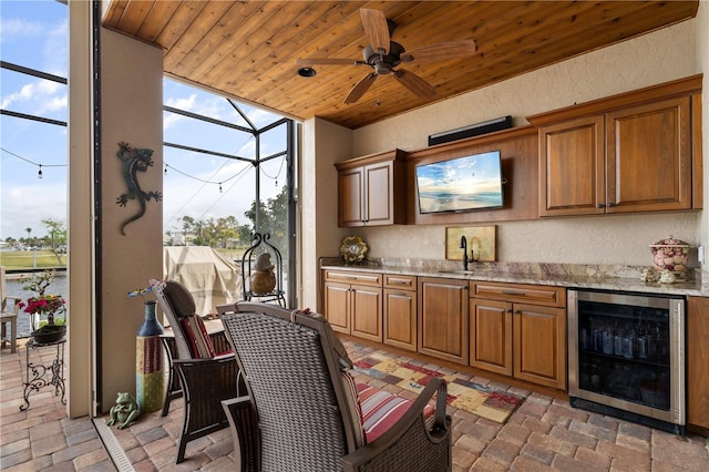 kitchen with light stone countertops, sink, ceiling fan, beverage cooler, and wooden ceiling