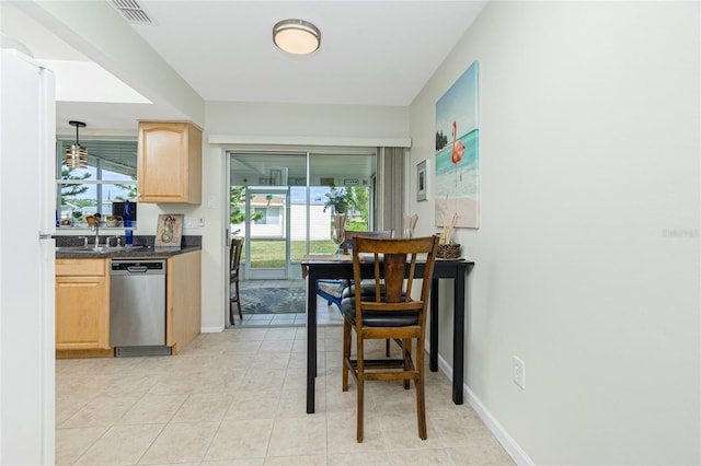 kitchen with light brown cabinetry, decorative light fixtures, stainless steel dishwasher, and a wealth of natural light