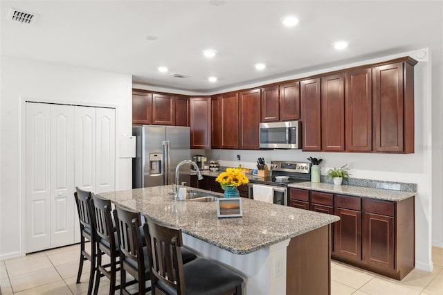 kitchen featuring sink, appliances with stainless steel finishes, a kitchen bar, light tile patterned floors, and a kitchen island with sink