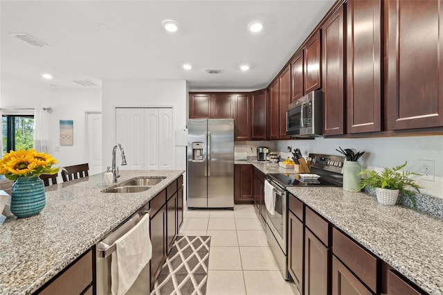 kitchen with stainless steel appliances, light tile patterned flooring, light stone countertops, and sink