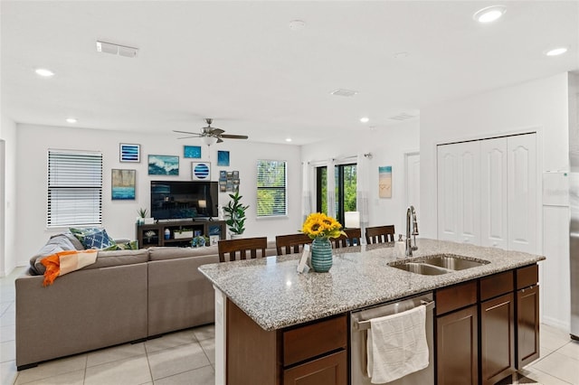 kitchen with a center island with sink, sink, light tile patterned floors, ceiling fan, and light stone countertops