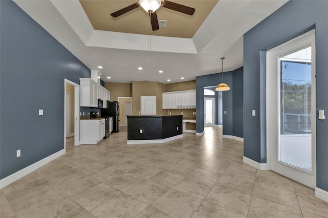 kitchen with pendant lighting, an island with sink, white cabinets, a raised ceiling, and a healthy amount of sunlight