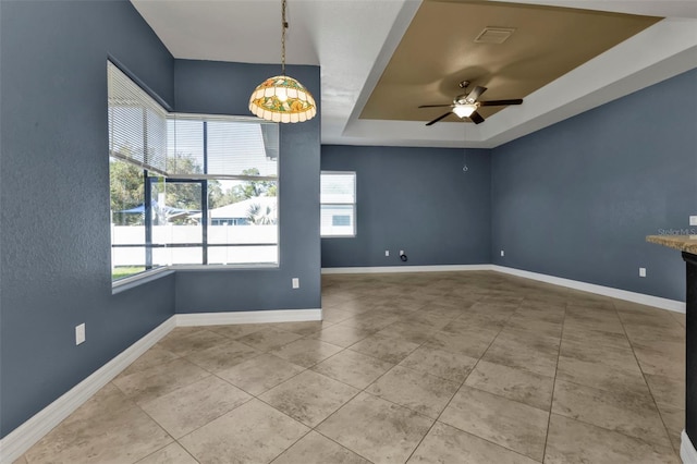 empty room featuring a raised ceiling, tile patterned floors, and ceiling fan