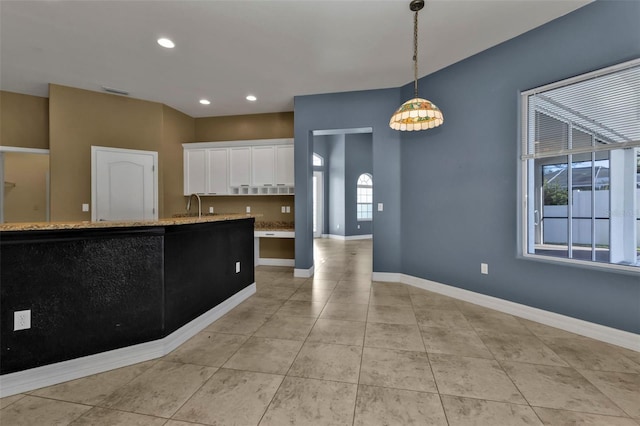 kitchen with sink, light tile patterned floors, light stone counters, white cabinets, and decorative light fixtures