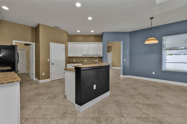 kitchen with sink, light stone countertops, white cabinets, black fridge, and decorative light fixtures