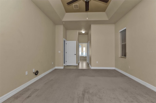 empty room with light carpet, a raised ceiling, and ceiling fan