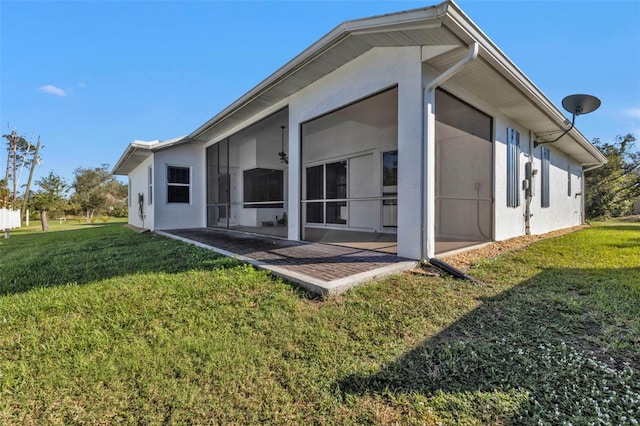 rear view of house featuring a lawn, a sunroom, and stucco siding