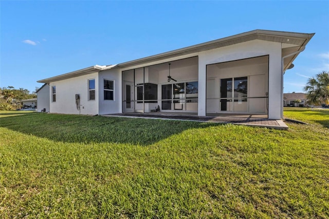 back of property featuring stucco siding, a lawn, and a sunroom