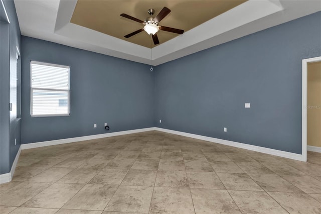 spare room with tile patterned flooring, ceiling fan, baseboards, and a tray ceiling