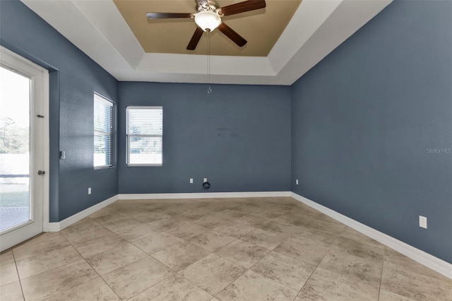 tiled empty room with a tray ceiling, baseboards, and a ceiling fan