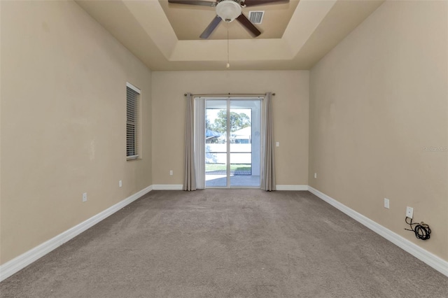 carpeted spare room featuring visible vents, baseboards, a tray ceiling, and a ceiling fan