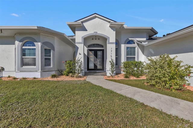 entrance to property with a yard, french doors, and stucco siding