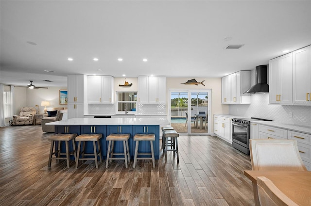 kitchen with stainless steel electric stove, wall chimney exhaust hood, and white cabinetry