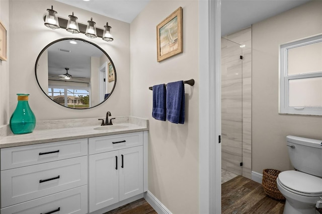 bathroom featuring hardwood / wood-style flooring, walk in shower, ceiling fan, vanity, and toilet