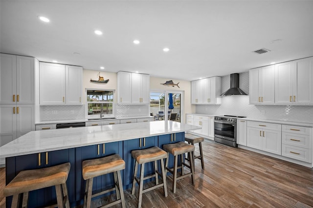 kitchen with a center island, stainless steel stove, wall chimney exhaust hood, and white cabinets