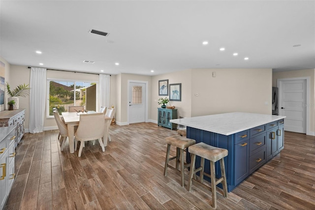 kitchen with blue cabinetry, a kitchen bar, stainless steel refrigerator, hardwood / wood-style flooring, and a center island