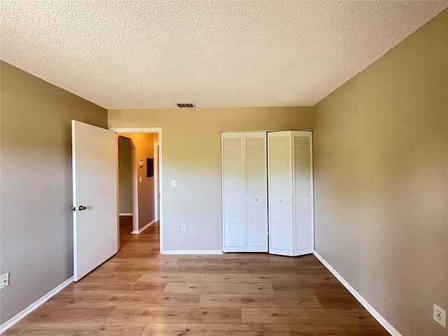 25068 Harborview Rd Unit 1A, Punta Gorda, FL 33980 - unfurnished bedroom with light wood-style floors, a closet, a textured ceiling, baseboards, and arched walkways