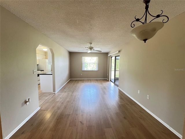 25068 Harborview Rd Unit 1A, Punta Gorda, FL 33980 - unfurnished living room featuring a textured ceiling, ceiling fan, wood finished floors, arched walkways, and baseboards