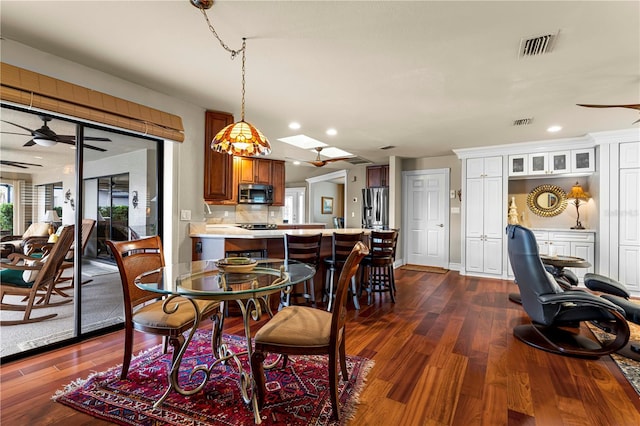 dining room with a skylight, ceiling fan, and dark wood-type flooring