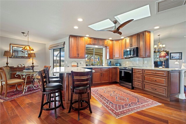 kitchen featuring pendant lighting, dark wood-type flooring, appliances with stainless steel finishes, a kitchen breakfast bar, and kitchen peninsula