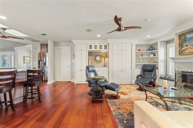 living room featuring a tile fireplace, ceiling fan, a skylight, dark hardwood / wood-style floors, and ornamental molding