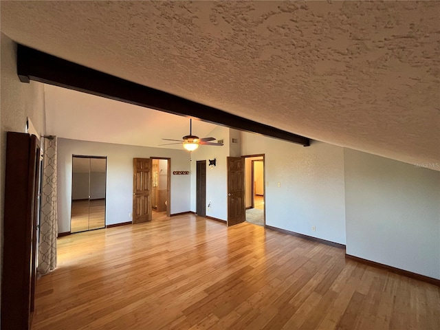 unfurnished living room with light wood-type flooring, a textured ceiling, lofted ceiling with beams, and ceiling fan