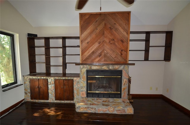 unfurnished living room with dark hardwood / wood-style floors, vaulted ceiling, and a stone fireplace