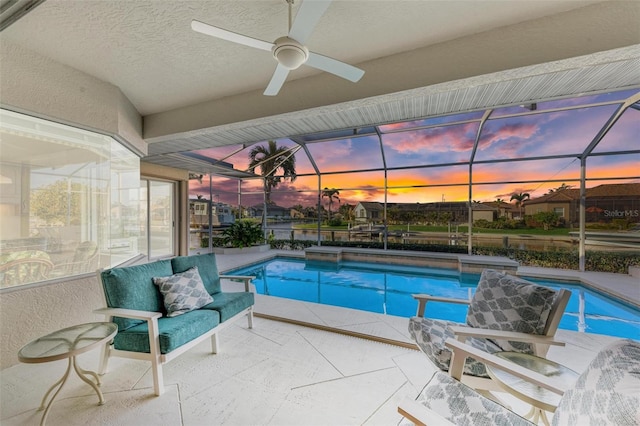 pool at dusk featuring a lanai, ceiling fan, and a patio