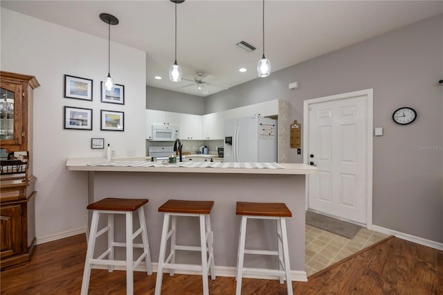 kitchen with white cabinetry, ceiling fan, kitchen peninsula, white appliances, and a kitchen bar