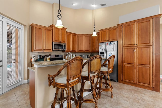 kitchen with light stone countertops, appliances with stainless steel finishes, pendant lighting, an island with sink, and light tile patterned flooring