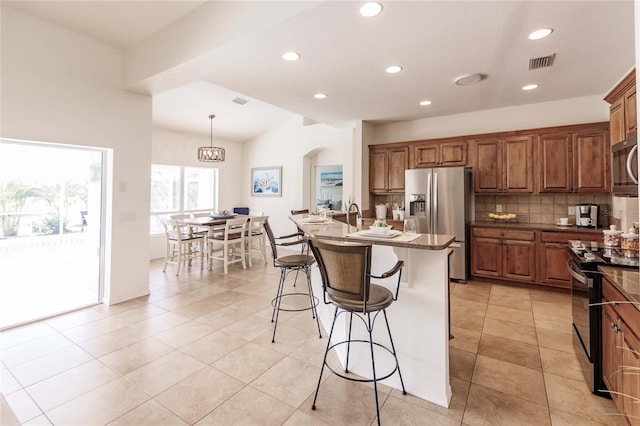 kitchen with tasteful backsplash, stainless steel appliances, decorative light fixtures, a center island with sink, and light tile patterned flooring