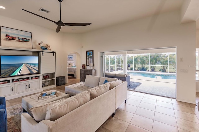 living room with ceiling fan, light tile patterned floors, and a high ceiling