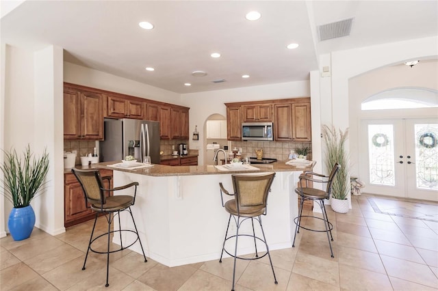 kitchen featuring a center island with sink, a breakfast bar area, appliances with stainless steel finishes, and french doors