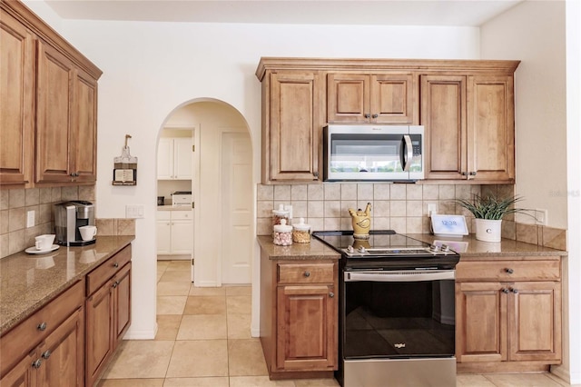 kitchen with stone countertops, decorative backsplash, light tile patterned floors, and appliances with stainless steel finishes