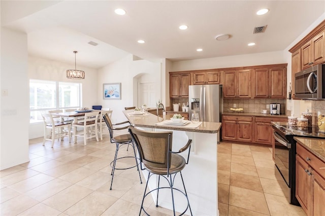 kitchen with stone counters, a center island with sink, decorative backsplash, decorative light fixtures, and stainless steel appliances