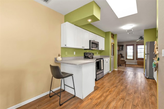 kitchen with a kitchen breakfast bar, a skylight, stainless steel appliances, hardwood / wood-style floors, and white cabinetry