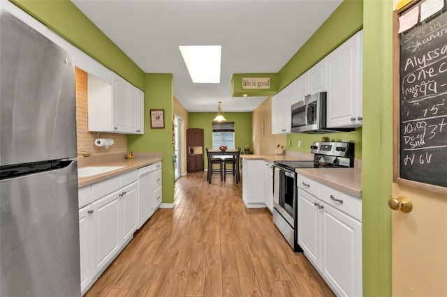 kitchen with white cabinets, appliances with stainless steel finishes, light wood-type flooring, and hanging light fixtures