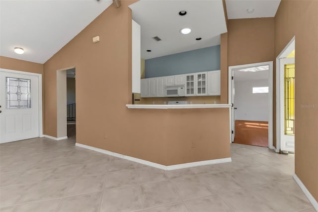 interior space with light tile patterned floors, white cabinetry, kitchen peninsula, and high vaulted ceiling