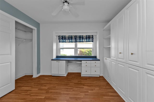 unfurnished office featuring light wood-type flooring, built in desk, and ceiling fan