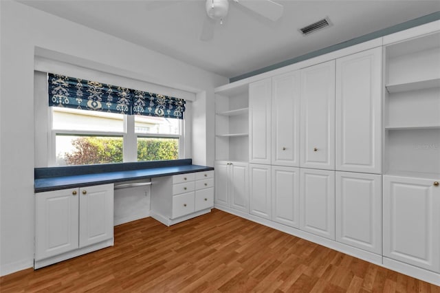 unfurnished office with ceiling fan, built in desk, and light wood-type flooring