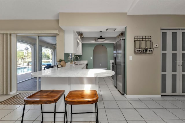 kitchen with white cabinets, stainless steel fridge, light tile patterned flooring, a kitchen bar, and kitchen peninsula