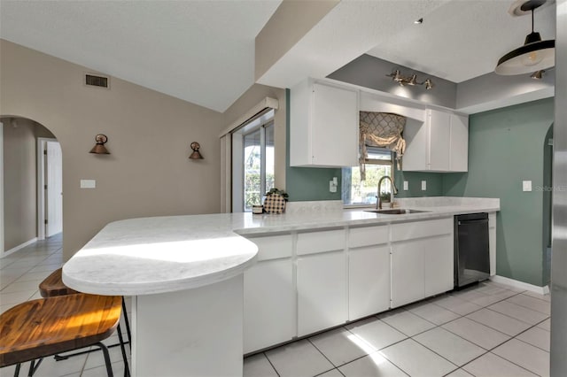 kitchen featuring dishwasher, lofted ceiling, white cabinets, sink, and light tile patterned floors