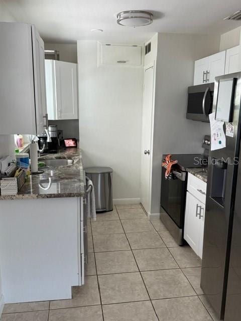 kitchen featuring appliances with stainless steel finishes, light tile patterned floors, white cabinetry, and dark stone countertops