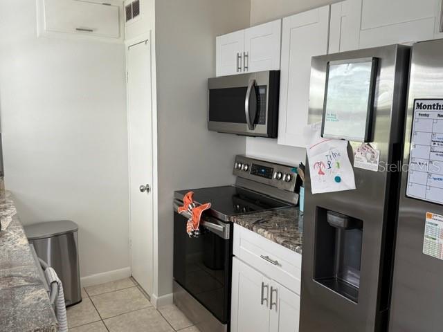 kitchen with dark stone countertops, white cabinets, light tile patterned flooring, and appliances with stainless steel finishes